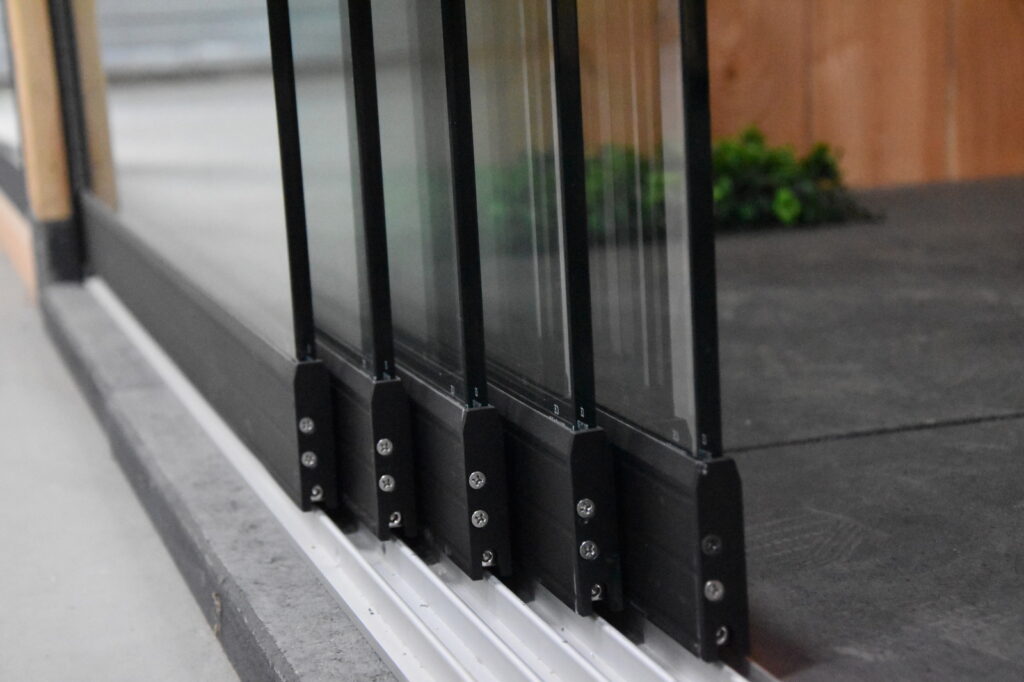 Nahaufnahme eines Aluminiumschienensystems für Glasschiebewände, mit mehreren beweglichen Paneelen auf der Schiene.