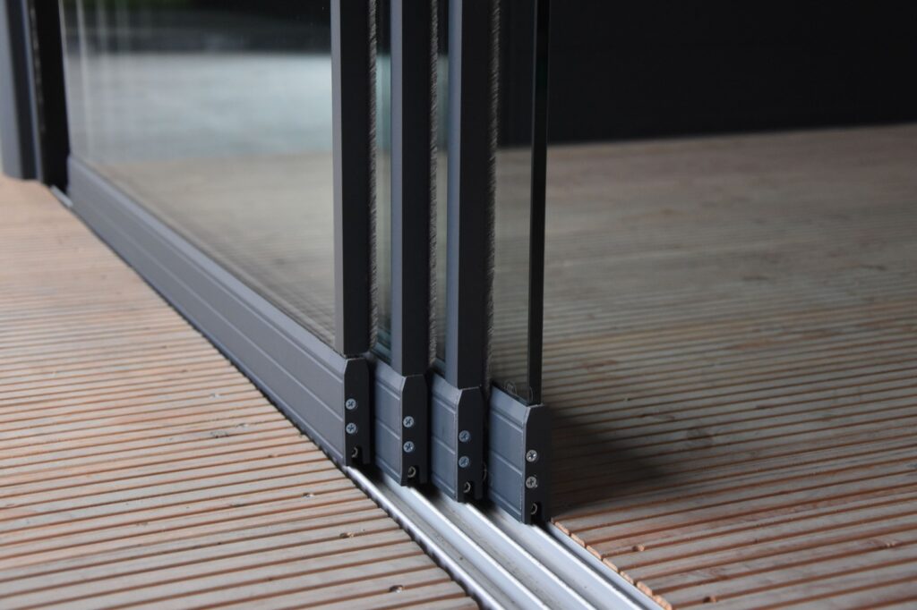 Detailaufnahme eines Glasschiebewandsystems auf einem Holzfußboden, mit robusten schwarzen Metallprofilen.