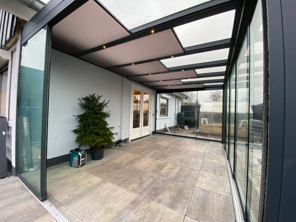 Moderner Wintergarten mit Glasschiebewänden und teilweise transparentem Dach mit integrierter Beleuchtung, ausgestattet mit gefliestem Boden und stilvoller Ausführung.