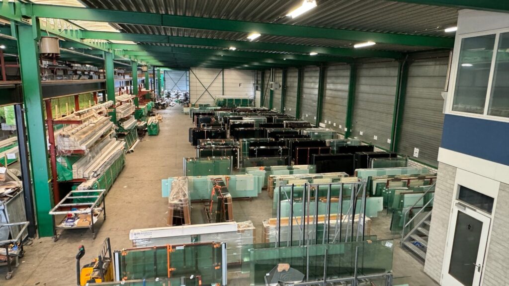 Innenansicht des Lagers von Jolie Patio mit großen Glasplatten und Aluminiumprofilen, ordentlich in Regalen aufbewahrt.