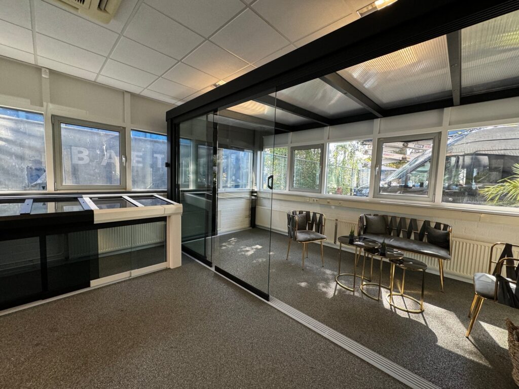 Gemütliche Showroom-Präsentation mit einer gläsernen Wintergarten-Konstruktion, ausgestattet mit einer stilvollen Sitzecke mit goldenen Akzenten.