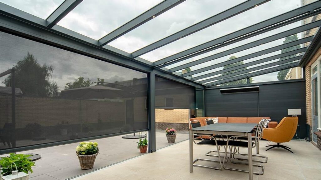 Überdachte Terrasse mit Glasdach und integrierten Reißverschlussmarkisen, eingerichtet mit Sitzecke und Esstisch, angrenzend an ein modernes Haus.